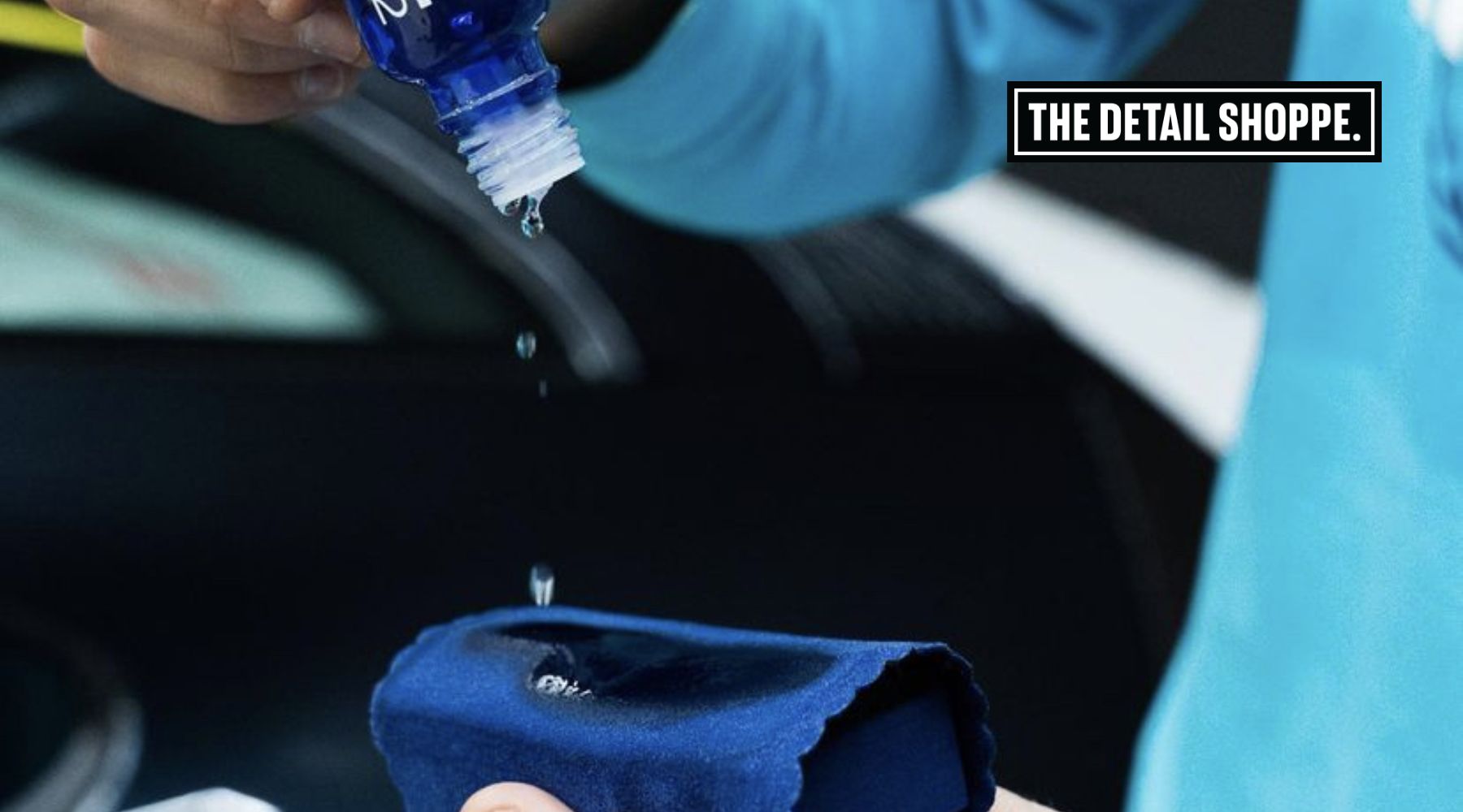 Close-up of a person applying ceramic coating onto a cloth, preparing to treat a vehicle at The Detail Shoppe. The bottle releases precise drops onto the applicator for even coverage.