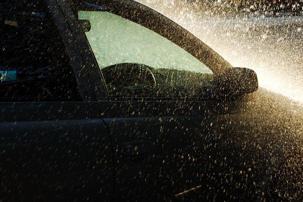 A car getting sprayed with water, illustrating how a protective coating like ceramic can resist water and grime buildup, even in heavy rain.