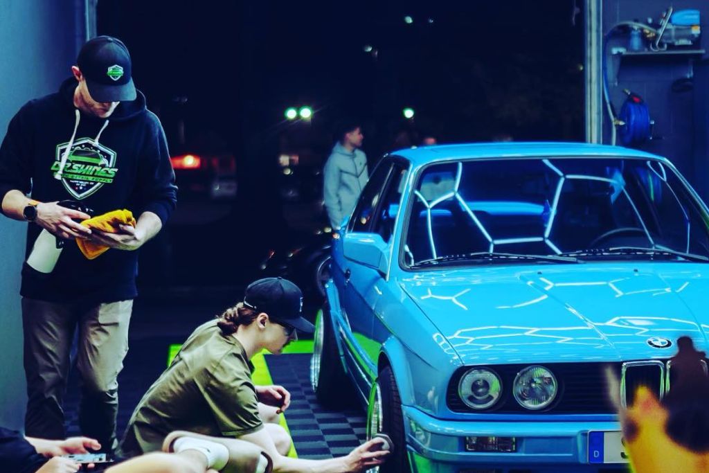 A team of detailers working on a blue car under bright lighting at The Detail Shoppe in Happy Valley, Oregon, applying ceramic coating for enhanced protection and shine.