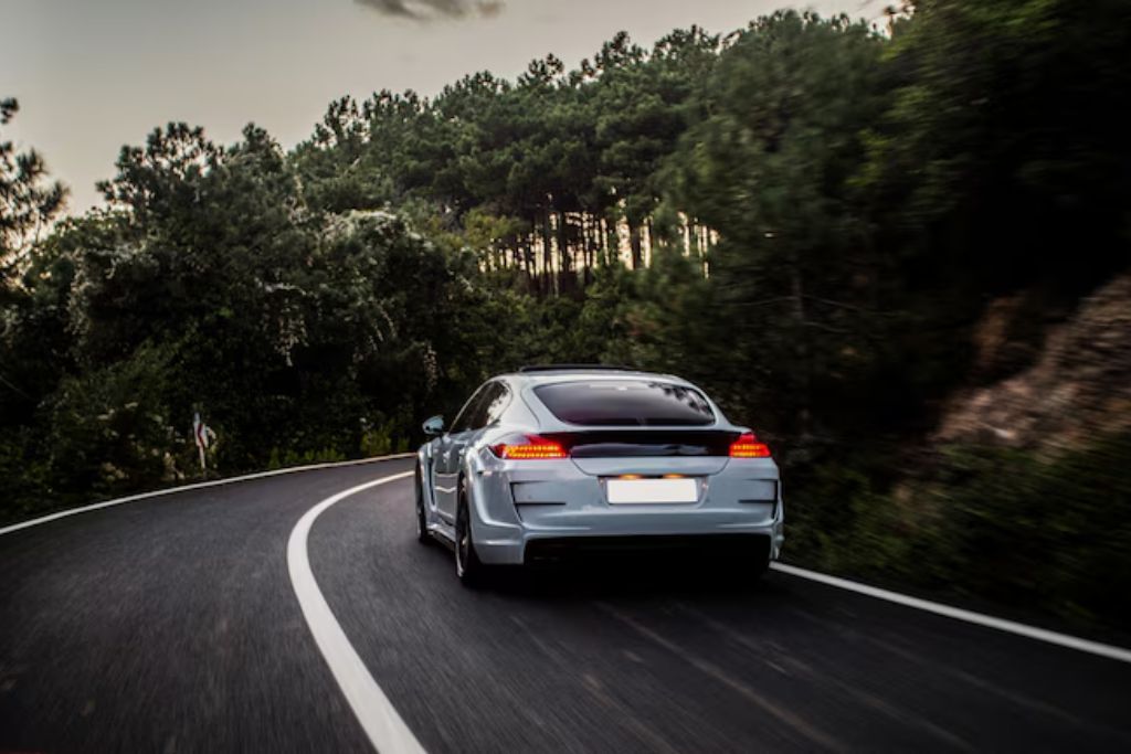 A sleek silver car drives along a winding, tree-lined road at sunset, emphasizing a clean, polished exterior and natural surroundings.