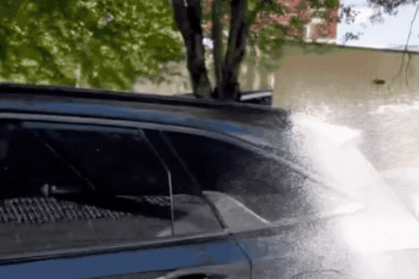 Water beads and sheets off the side of a dark SUV as it’s sprayed, demonstrating the hydrophobic effect of well-maintained paint protection film in action under natural light.