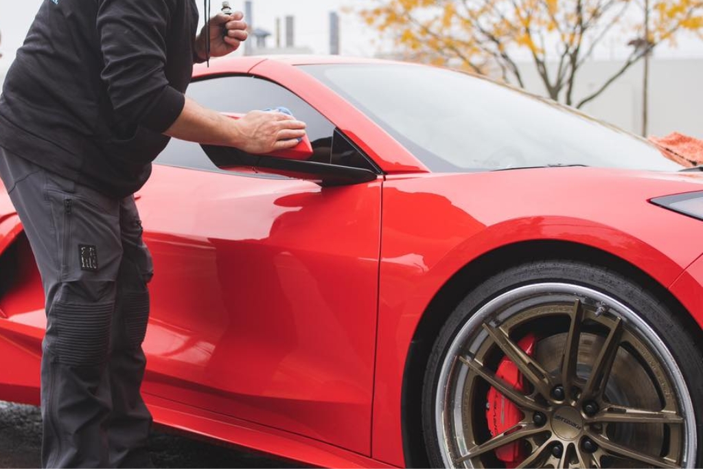 Detailer applying ceramic coating to the side mirror of a red sports car outdoors in Happy Valley during fall, demonstrating that yes, you can reapply ceramic coating outdoors in autumn with the right weather conditions.