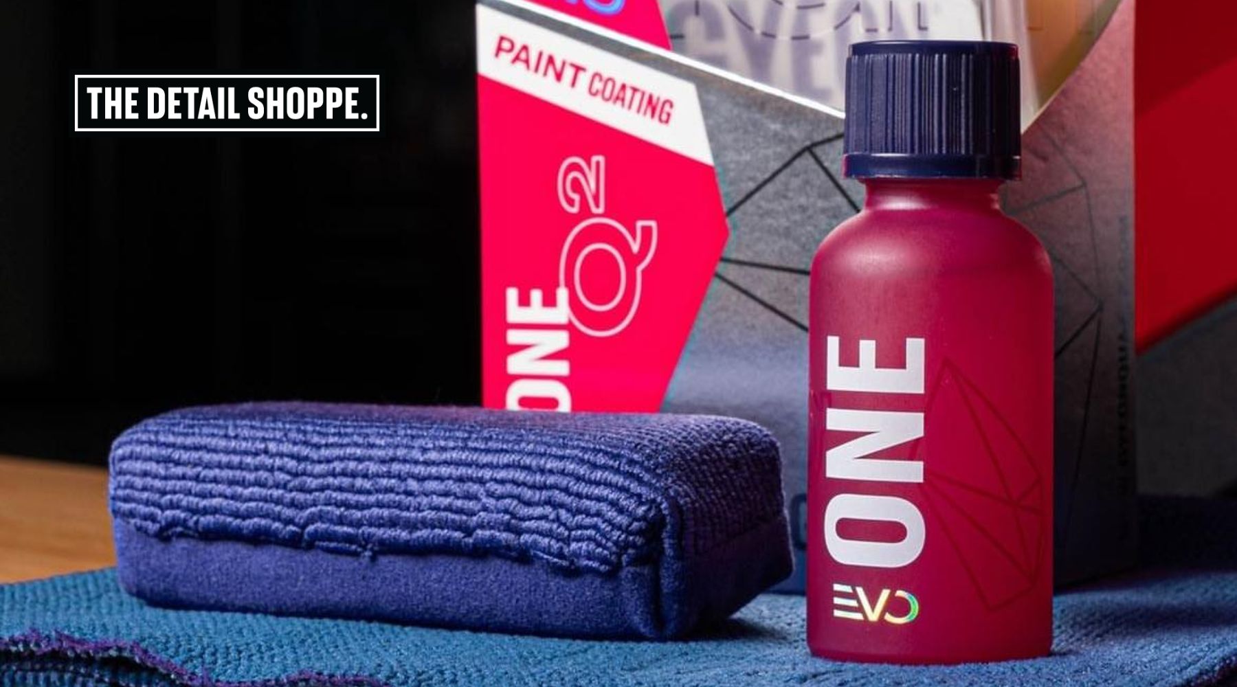 Close-up of a ceramic coating kit from The Detail Shoppe in Happy Valley, Oregon, featuring a red EVO ONE paint coating bottle, blue microfiber towels, and product packaging. This image supports the discussion on whether ceramic coating is worth it for new cars in Happy Valley.
