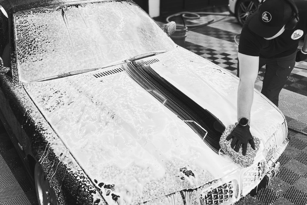 Detailer hand-washing a foam-covered car hood at The Detail Shoppe, demonstrating proper technique as part of essential winter maintenance tips to preserve ceramic coating performance.