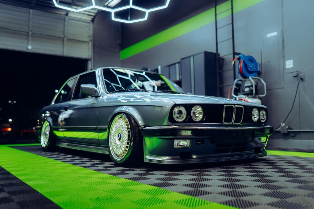 A freshly detailed dark gray BMW with a high-gloss ceramic coating sits indoors on a vibrant green and black checkered floor. The flawless reflection on the body emphasizes why understanding how long before rain after coating is essential for preserving a perfect finish, especially in humid regions like Happy Valley.