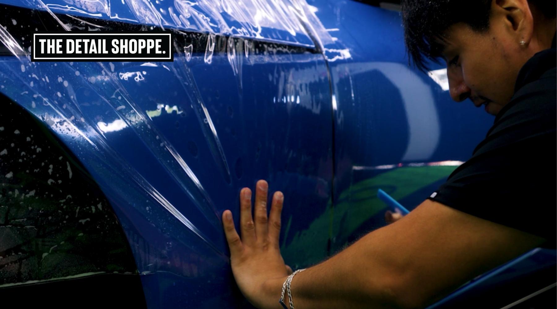 A detailing specialist from The Detail Shoppe applies clear paint protection film to a shiny blue car in Happy Valley, OR. This image highlights the process involved in answering the question: How Long Does Paint Protection Film Last in the Pacific Northwest’s wet and variable climate.