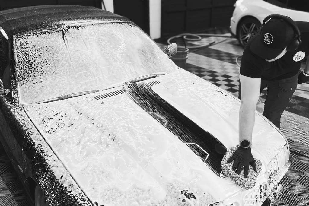 A detailing technician from The Detail Shoppe in Happy Valley, OR hand washes a car covered in thick foam using a soft mitt, emphasizing gentle care practices. This image supports the importance of proper aftercare to maximize the lifespan of paint protection film and maintain its performance over time.