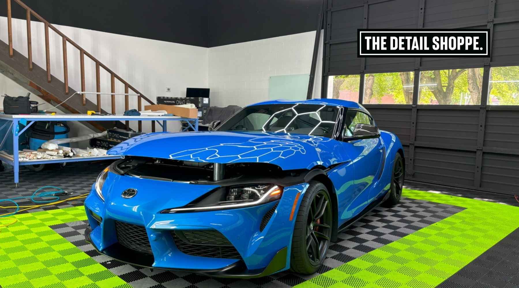 Blue Toyota Supra parked inside The Detail Shoppe’s garage in Happy Valley, OR, with visible Paint Protection Film on the hood and high-gloss reflections from overhead lighting, illustrating a professional PPF application.