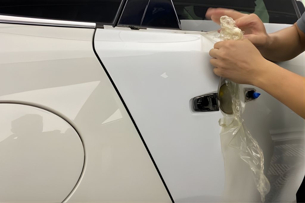 Close-up of a technician carefully peeling off old paint protection film from the door panel of a white vehicle at The Detail Shoppe in Happy Valley, OR. This image visually answers the question when should PPF be replaced, highlighting the removal process when film begins to show wear or lose effectiveness.