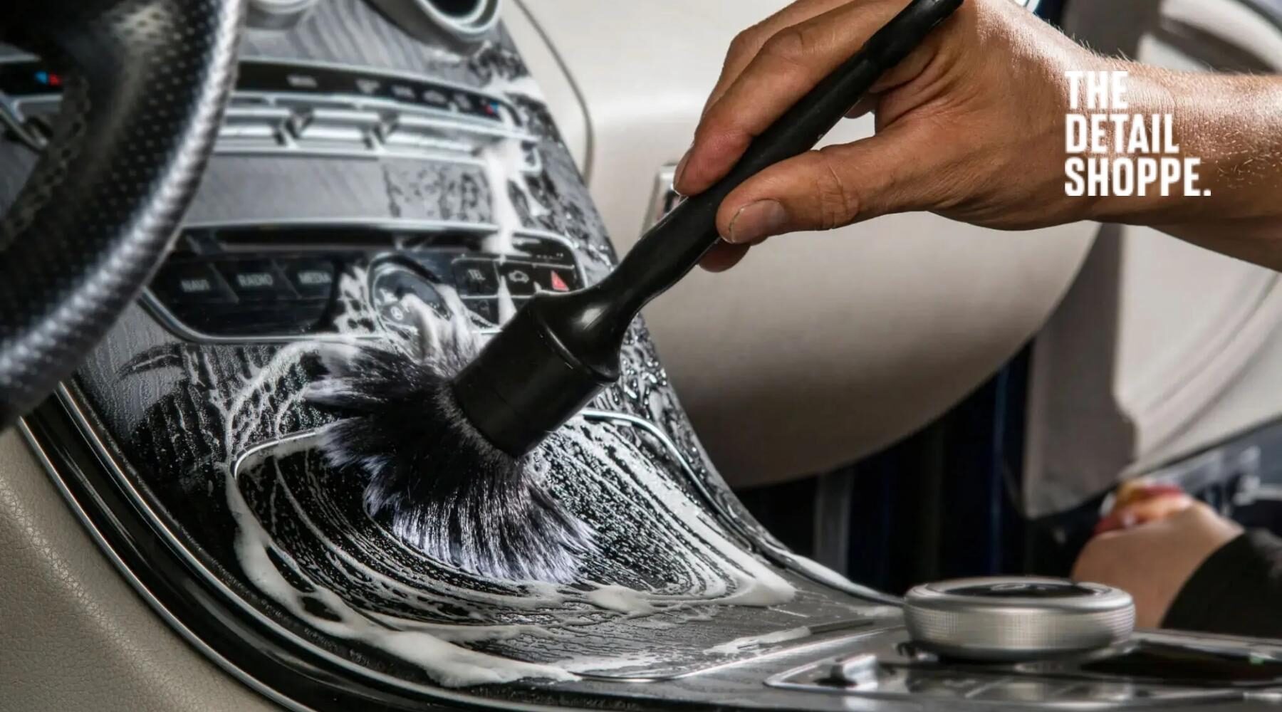 Professional auto detailer deep cleaning a car's center console with a soft bristle brush and foaming cleaner.