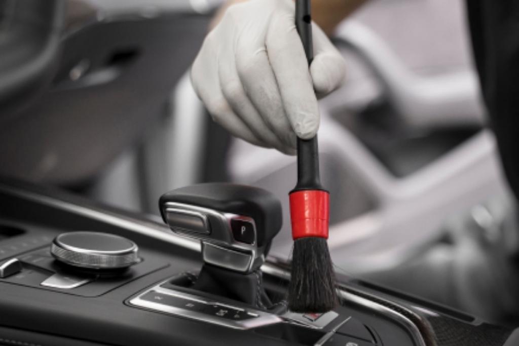 Detailing technician using a soft brush to clean around the gear selector in a luxury vehicle interior.