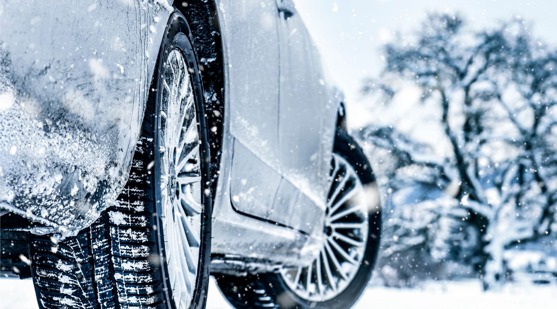 Close-up of a silver car with snow-covered tires parked in a snowy environment, promoting exterior car detailing services for winter protection against rain, mud, and contaminants in Happy Valley.