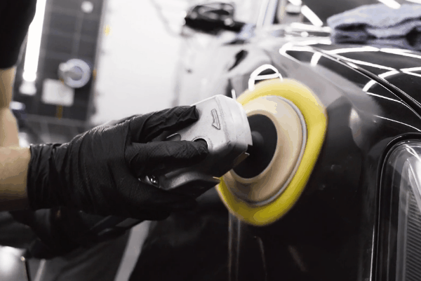 Auto detailing specialist polishing a black vehicle with a dual-action buffer during paint correction.
