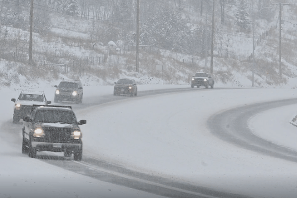 Several vehicles drive cautiously on a snow-covered, winding road during active snowfall in Happy Valley, highlighting the harsh winter conditions that contribute to vehicle exterior damage from moisture, road treatments, and grime buildup.