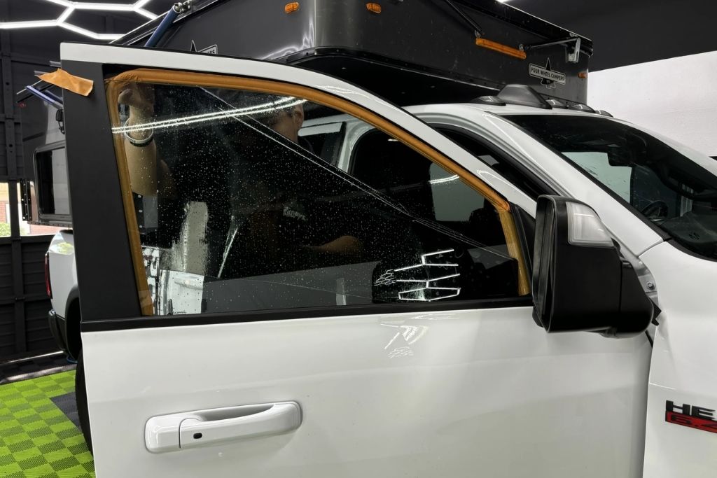 Window tint film being carefully applied to a white truck door window inside The Detail Shoppe in Happy Valley, Oregon.