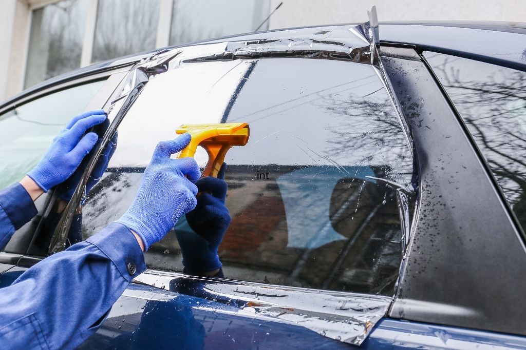 Technician using a squeegee to apply window tint film to a car’s rear passenger window for a smooth, bubble-free finish.