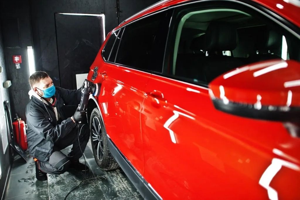 Technician polishing a red SUV with a machine buffer during professional car detailing service in Happy Valley, OR