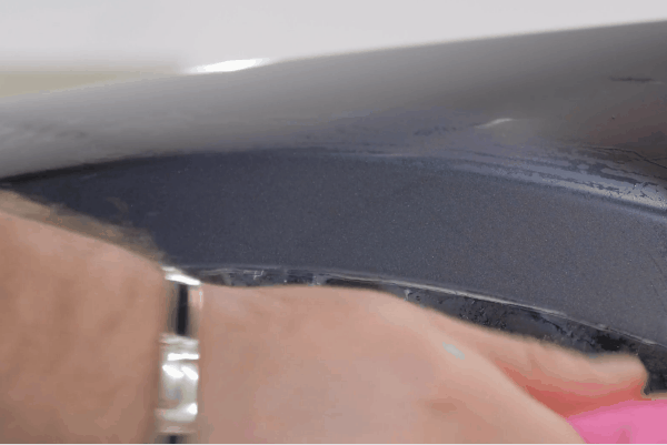 Technician using a pink squeegee tool to smooth paint protection film onto a vehicle surface during installation.