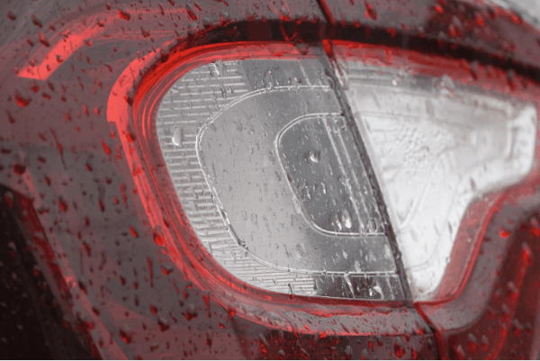 Close-up of a car tail light with rain droplets beading on the surface after ceramic coating protection.