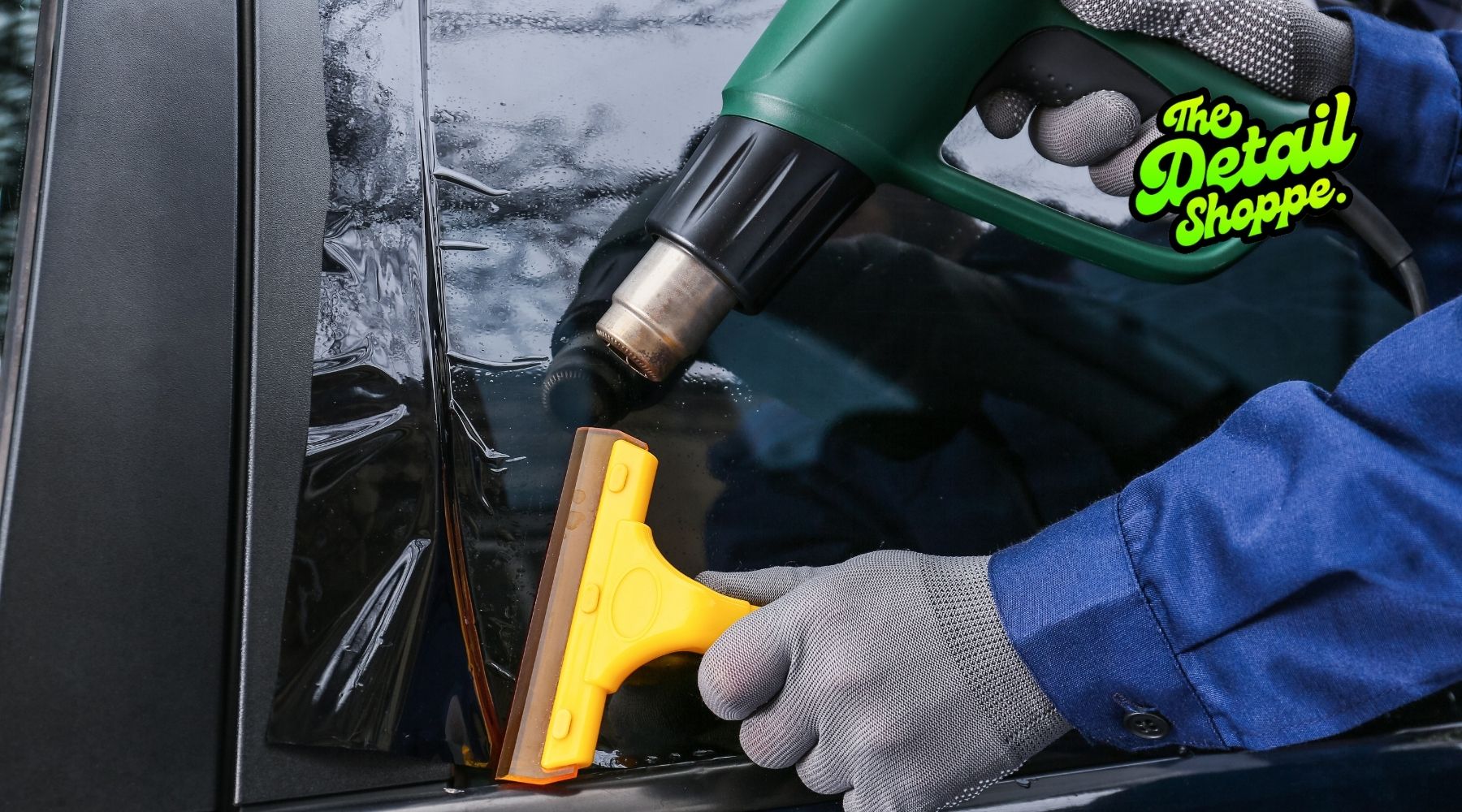 Technician applying car window tint with a heat gun and squeegee at The Detail Shoppe