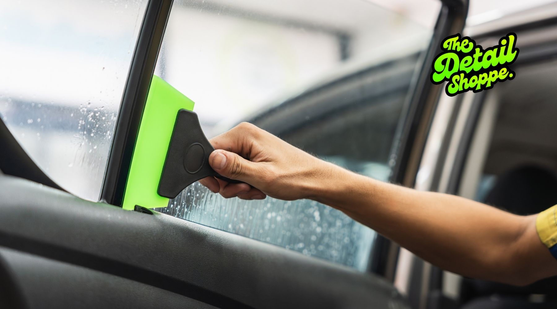 Technician applying window tint film to a car door window with a squeegee at The Detail Shoppe