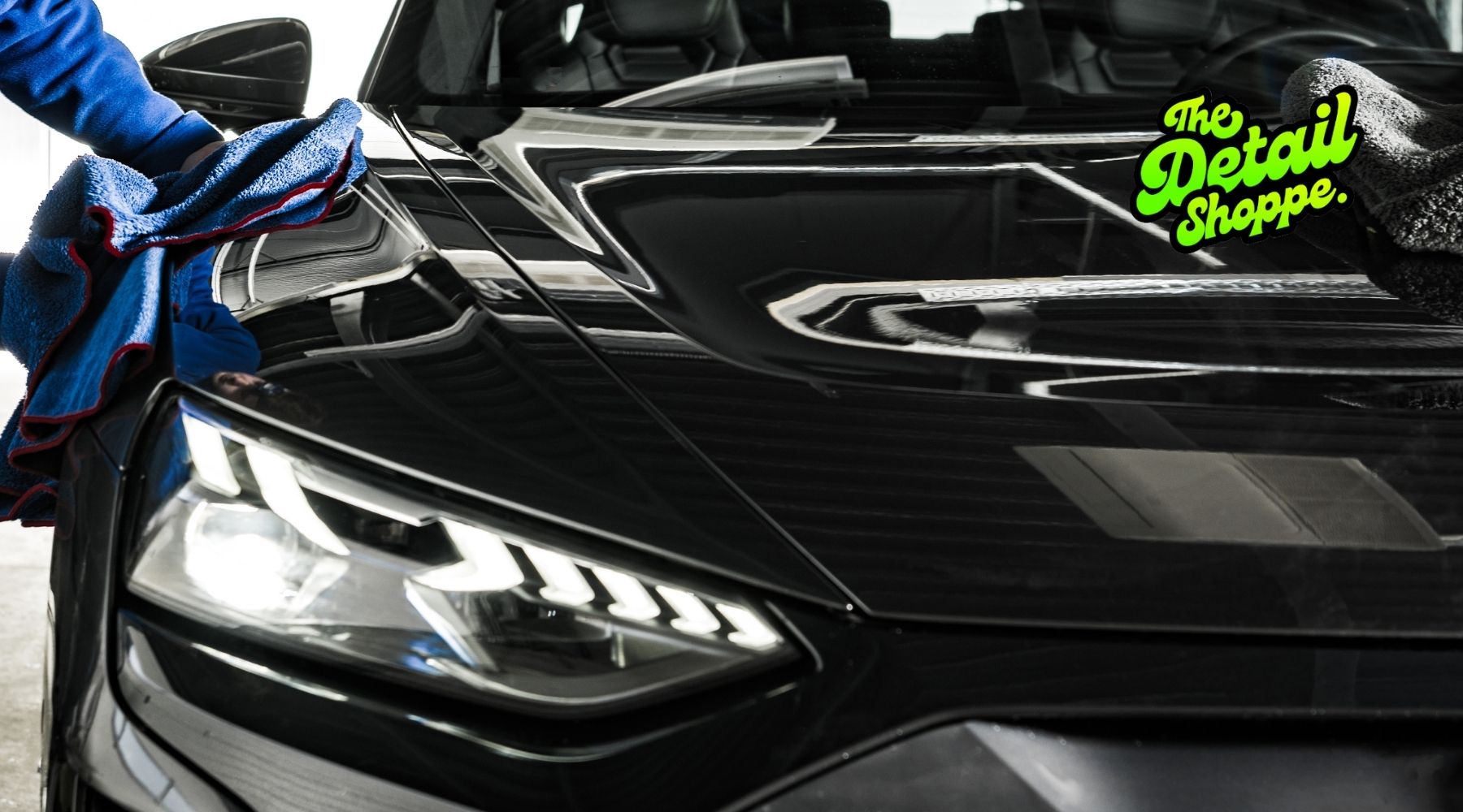 Person wiping the hood of a black car during professional auto detailing at The Detail Shoppe