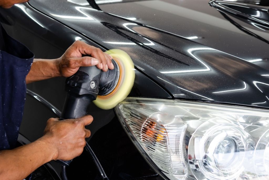 Technician polishing a black car panel with a machine buffer during paint correction detailing