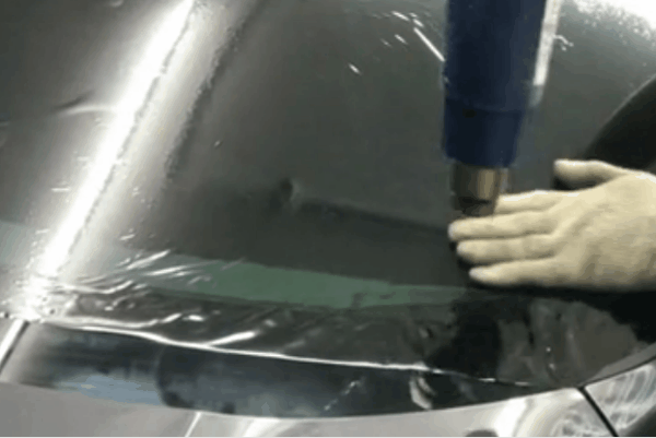 Technician hand smoothing dark window tint film onto a rear vehicle window during installation