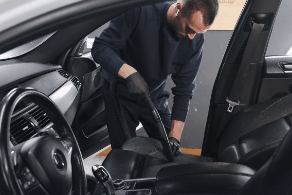 Technician vacuuming a car seat and interior cabin during professional interior auto detailing service