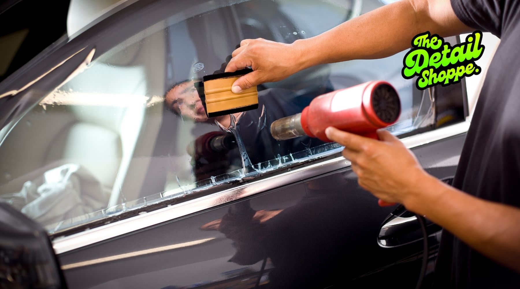 Technician applying car window tint film using heat gun and squeegee during professional installation