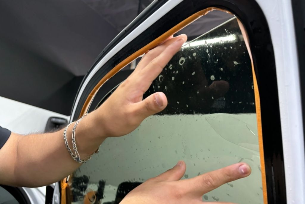 Close-up of technician smoothing car window tint film during installation on vehicle glass