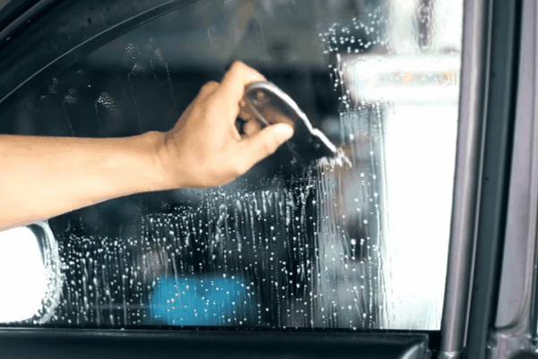 Technician smoothing ceramic window tint film with squeegee on car window for bubble-free installation